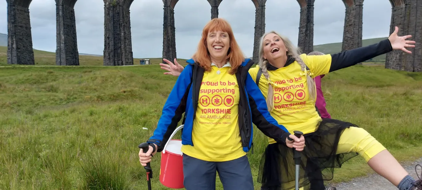 Dos excursionistas con camisetas amarillas, con el viaducto de Ribblehead a sus espaldas.