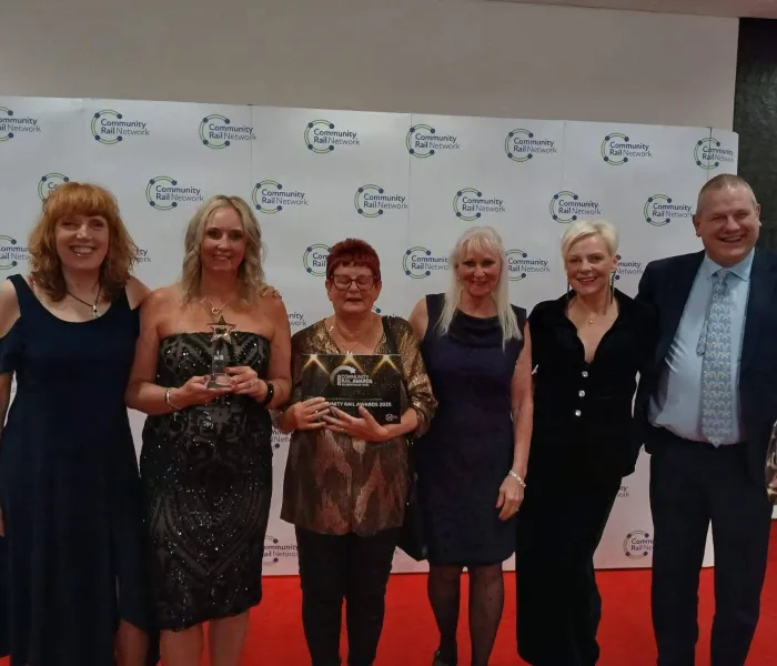 5 Frauen und ein Mann mit einer Auszeichnung in Form eines Banners mit der Aufschrift „Community Rail Awards 2025“